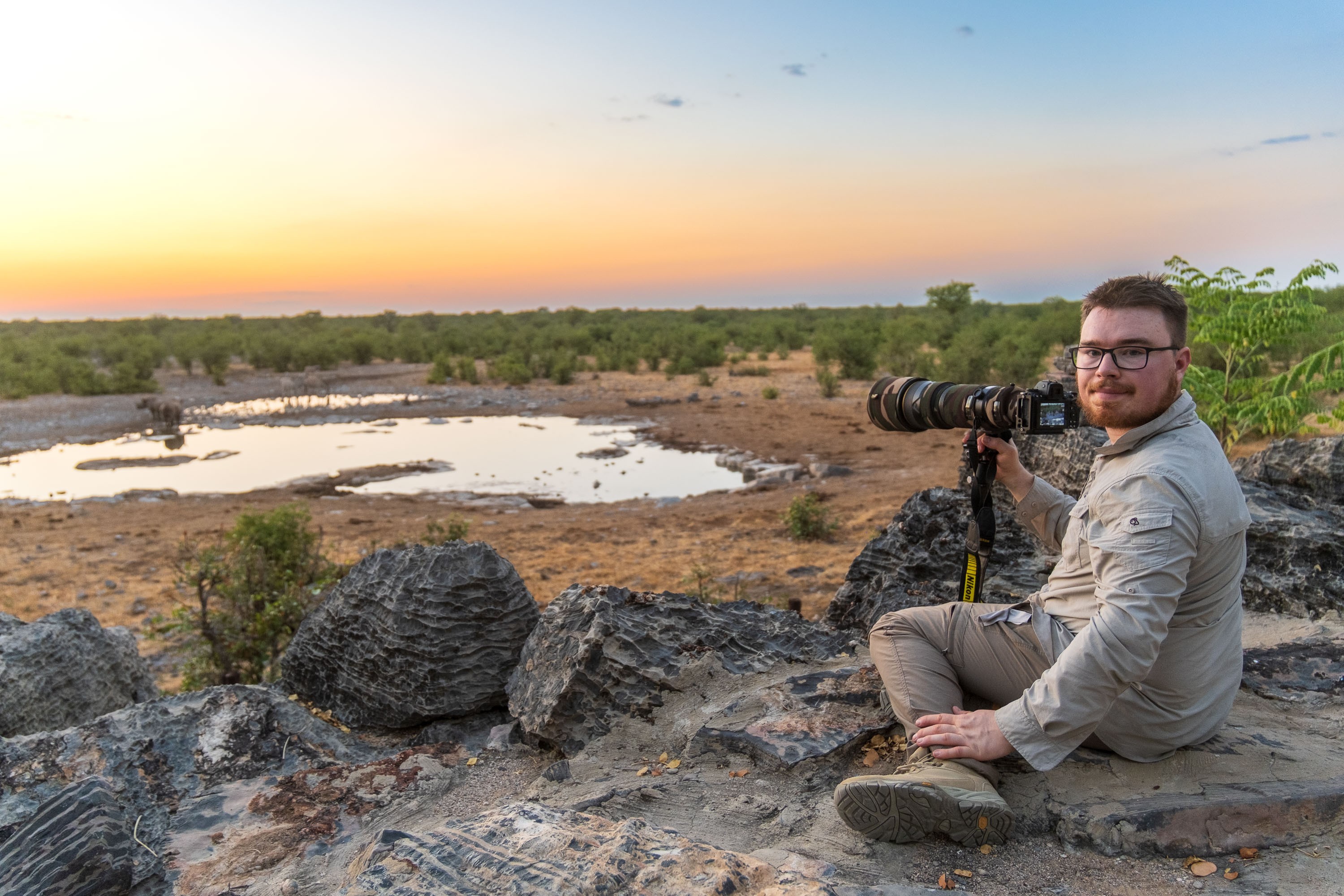 Reisefotograf Felix Lukas Kübler sitzt am Wasserloch in Namibia mit Nikon 200–400mm F4 und wartet bei Sonnenuntergang auf Wildtiere.